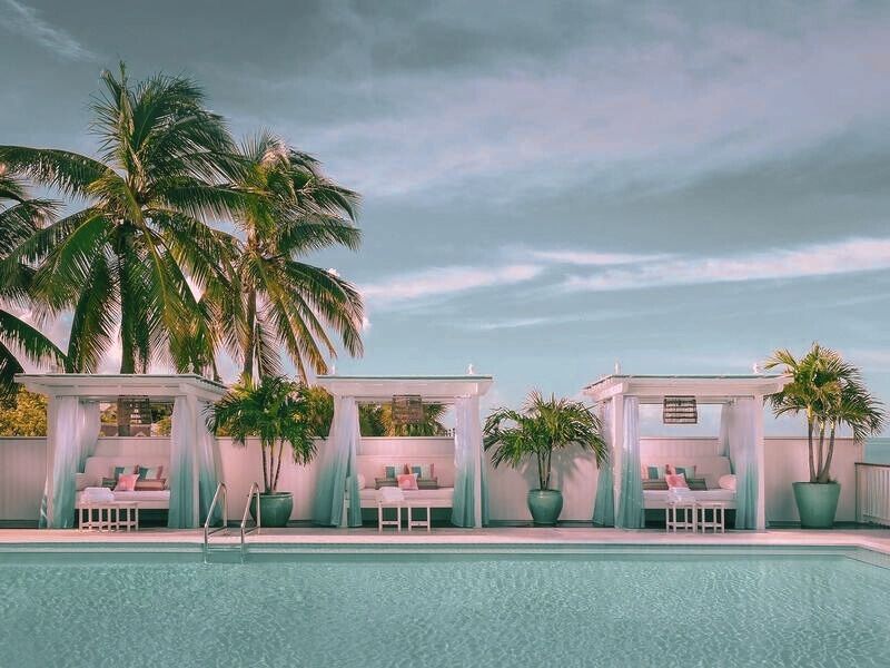 A beautiful pool at the beach club hotel in Miami, bordered by tall palm trees and cabanas. The clear water reflects the blue sky, creating a beautiful atmosphere perfect for relaxation.
