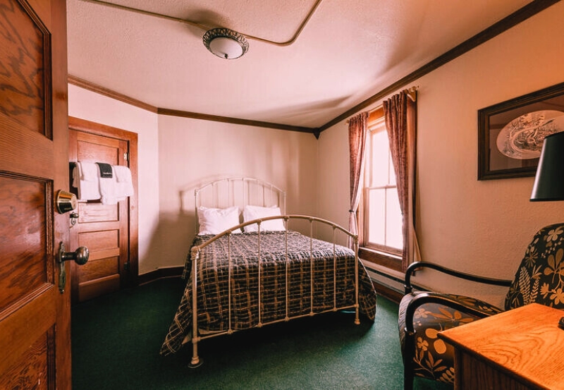 A cozy bed in a room featuring a window and a chair, set in the haunted Chico Hot Springs Resort & Day Spa.