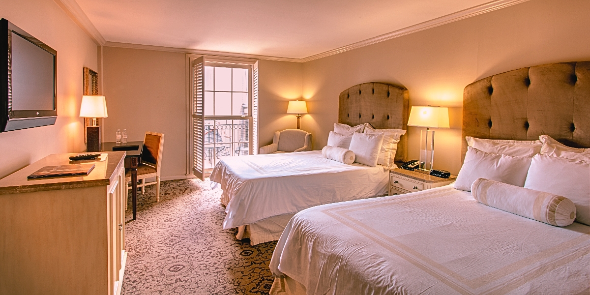 Two beds and a television in a hotel room, highlighting the charm of the Dauphine Orleans Hotel, a historic site near Bourbon Street.