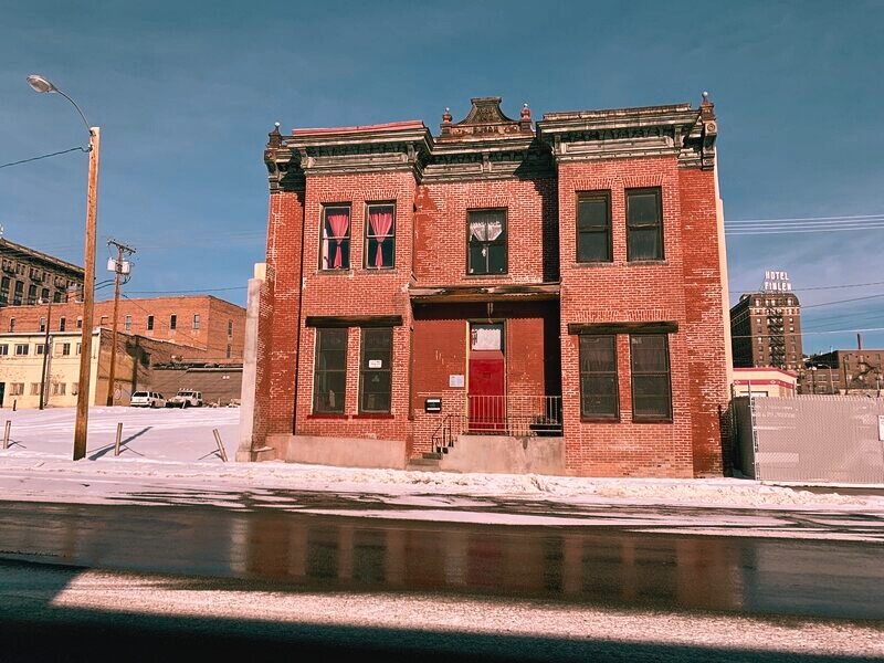 Old brick structure featuring a red door, the Dumas Brothel, a former brothel turned museum in Butte, rich in history and haunted spots.