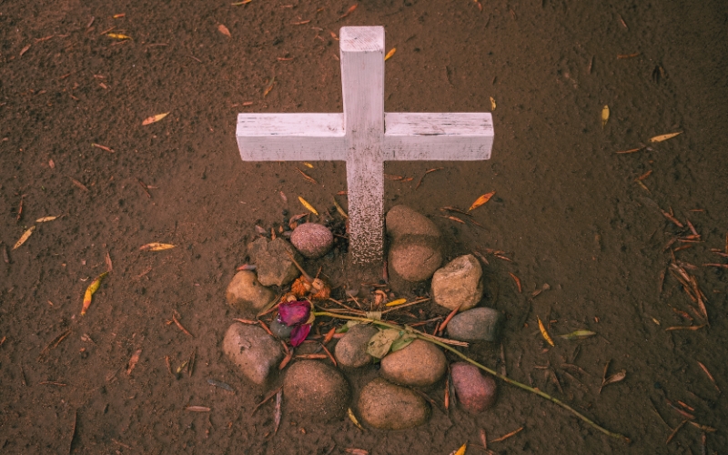 A cross and stones arranged on the ground at El Campo Santo Cemetery in San Diego, symbolizing remembrance and peace.