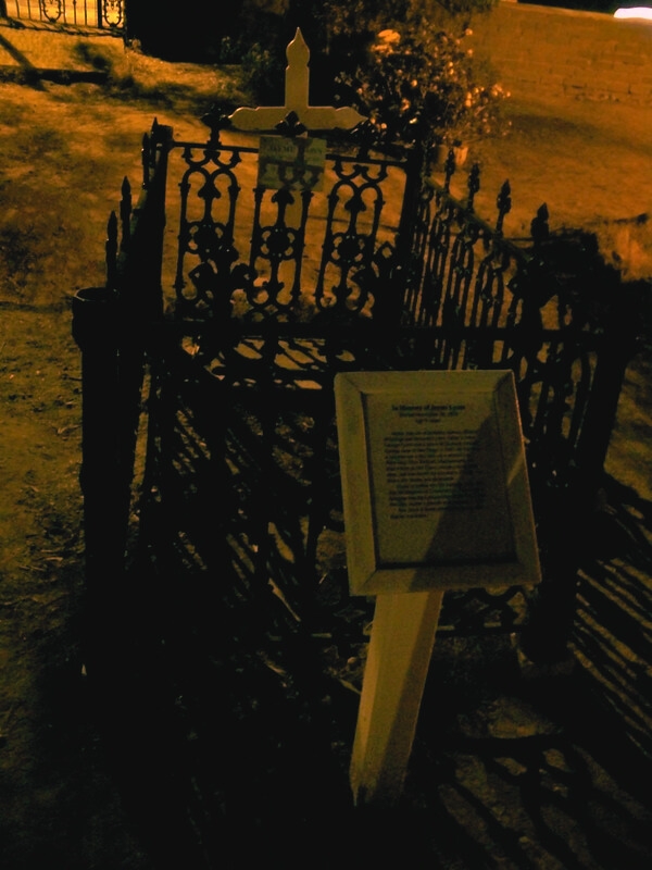 A nighttime view of a grave in the haunted El Campo Santo Cemetery, San Diego, featuring a sign placed at the headstone.