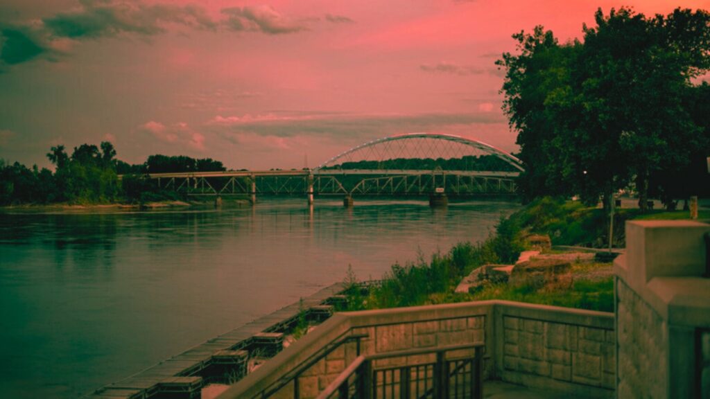 The Missouri River flows beneath a bridge, framed by lush trees in the background, highlighting a tranquil landscape, near one of the most haunted places in Atchison Kansas.