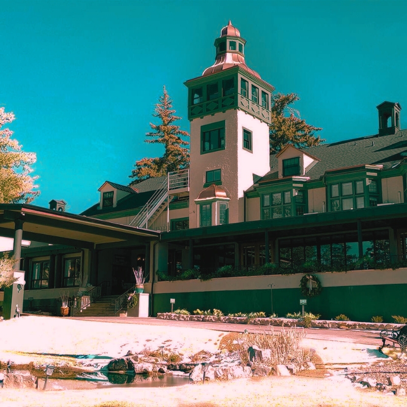 A large white Victorian building with a clock tower, sits among towering pine trees in the Sacramento Mountains.