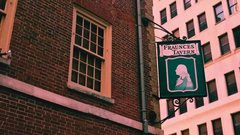 The sign for Fraunces Tavern, a historic bar, prominently featured on a building, beckoning visitors to its Revolutionary War heritage.