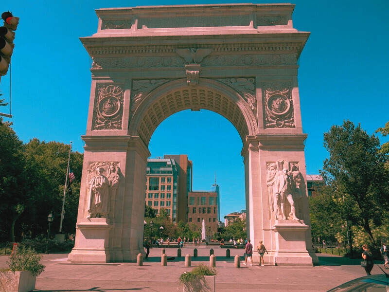 The grand arch with statues atop, symbolizing the lively yet haunted history of Washington Square Park in New York City.