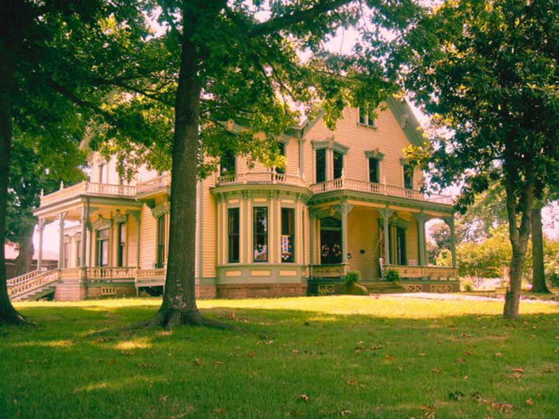 A large yellow house with green trim, surrounded by trees, known as the haunted Clayton House.