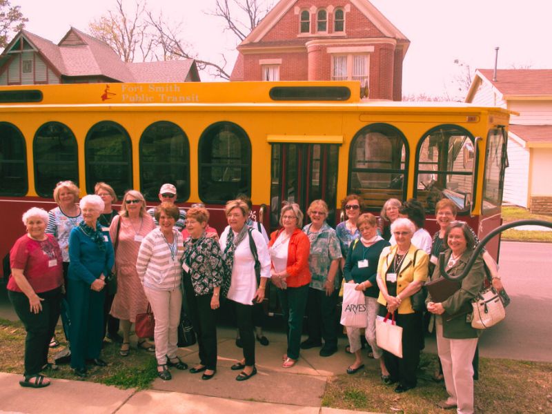 A group of individuals poses by a bus, with the haunted Clayton House behind them, hinting at a ghostly adventure.