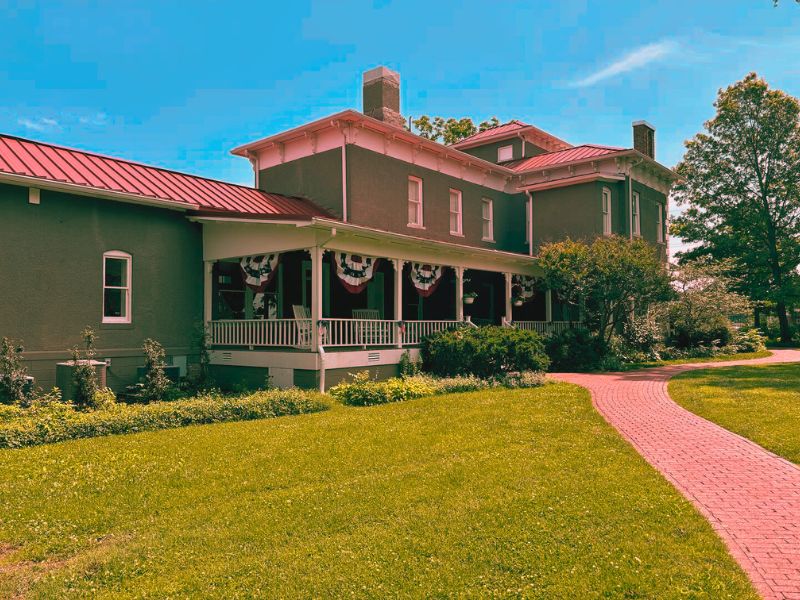 A large house with a red roof, known as the haunted Peel Mansion, surrounded by trees and a cloudy sky.