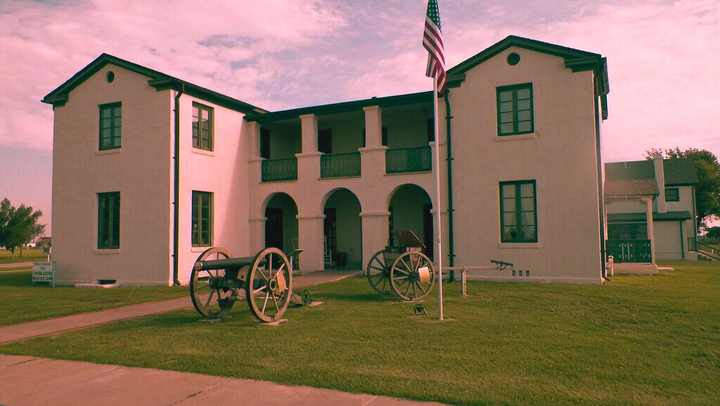 A large white building at Fort El Reno, featuring two cannons on the lawn, known as one of Oklahoma's most haunted sites.