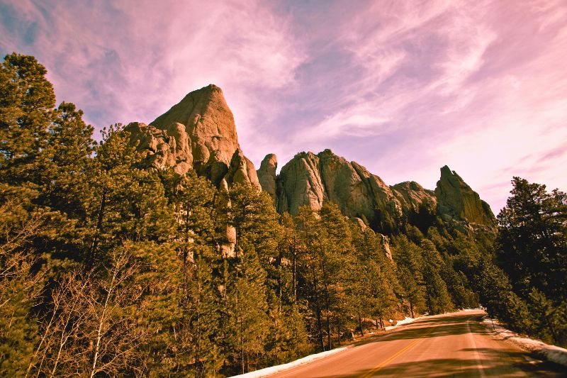 A winding road with impressive rock formations in the background, set in the Black Hills, South Dakota.