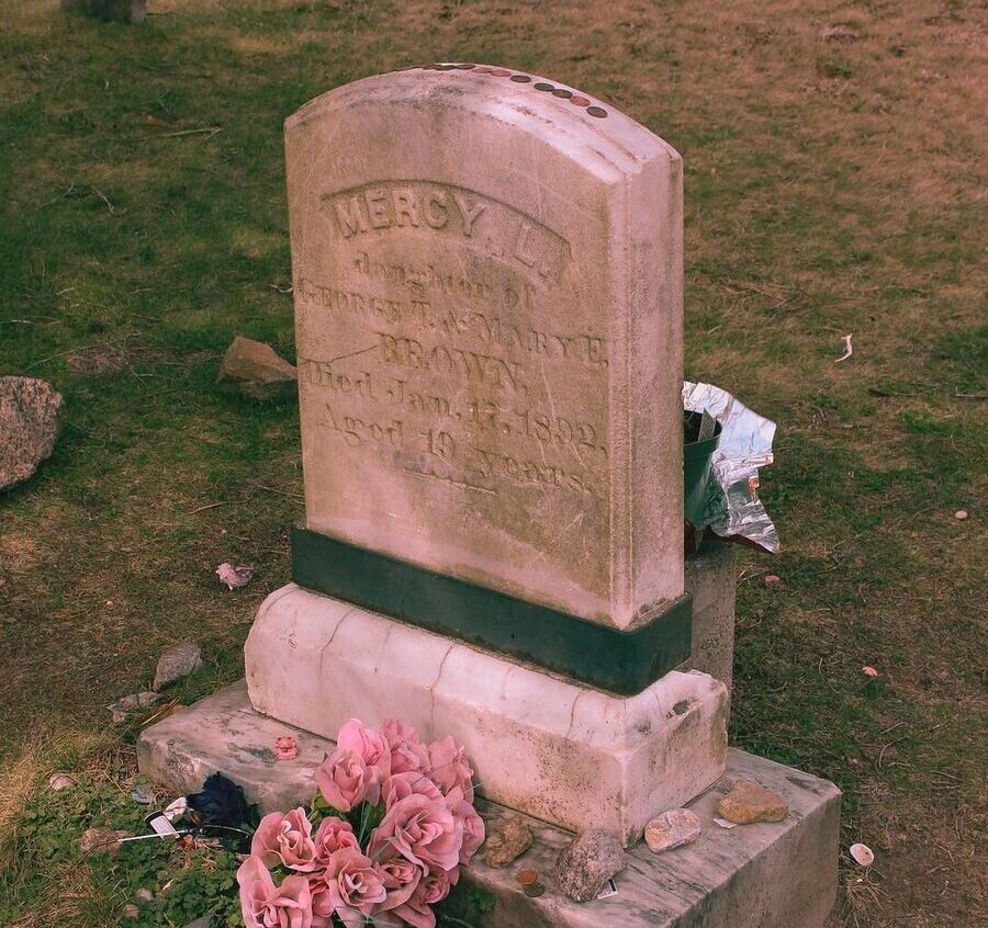 Tombstone of Mercy Brown, surrounded by flowers, at her grave in one of Rhode Island's most famous supernatural locations.