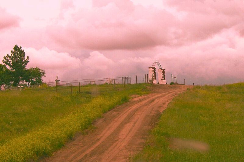 A dirt road winds up to a white church on a hill, located at the Wounded Knee Massacre Site, a haunted place in South Dakota.